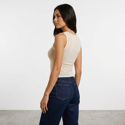 Woman in a sleeveless top and jeans, posing side view.
