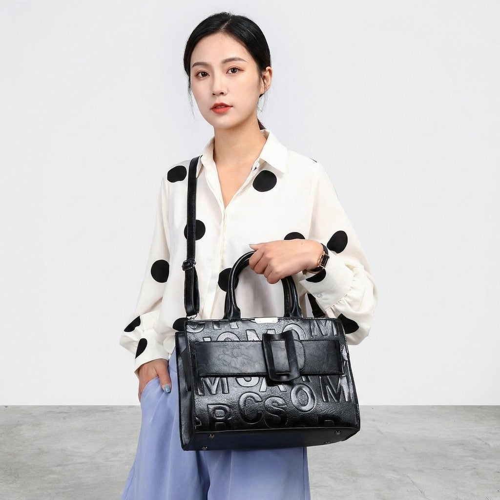 Person in polka-dot blouse holding a stylish black handbag.