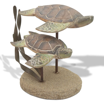 Two wooden turtles swimming on a sandy base with seaweed.