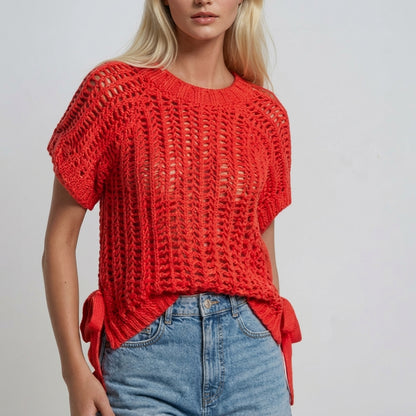 Blonde woman in red crochet top and blue jeans against a plain background.