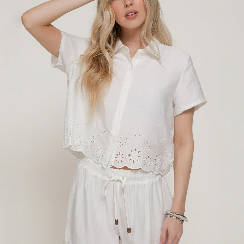 Woman in white floral outfit, posing with hand in hair.