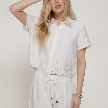 Woman in white floral outfit, posing with hand in hair.