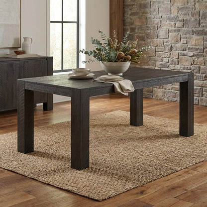 Dark wooden table with vase and dishware on woven rug, brick wall backdrop.
