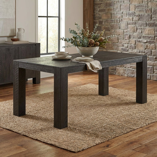 Dark wooden table with vase and dishware on woven rug, brick wall backdrop.