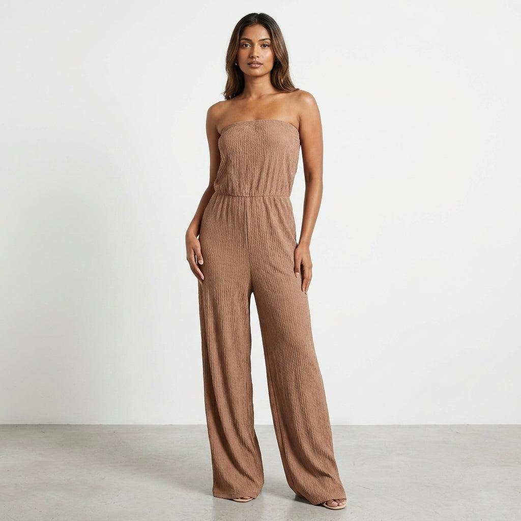 Woman in a strapless beige jumpsuit standing on a plain background.