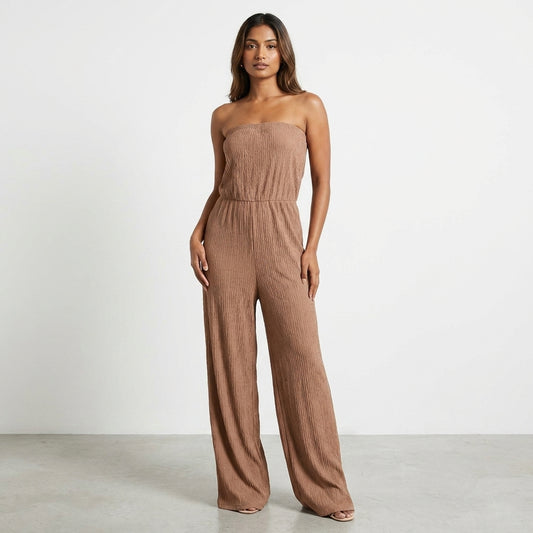 Woman in a strapless beige jumpsuit standing on a plain background.
