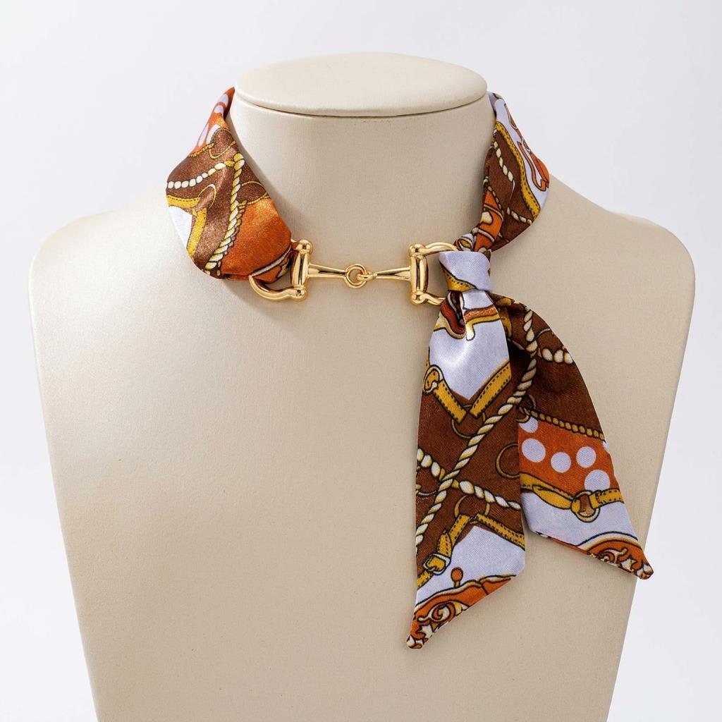 A patterned silk scarf fastened with a gold-tone clasp is displayed on a mannequin.