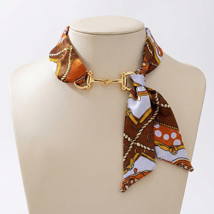 A patterned silk scarf fastened with a gold-tone clasp is displayed on a mannequin.