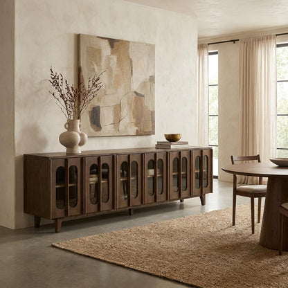 A warm, minimalist dining room with a dark wood sideboard, abstract art, and natural textures.