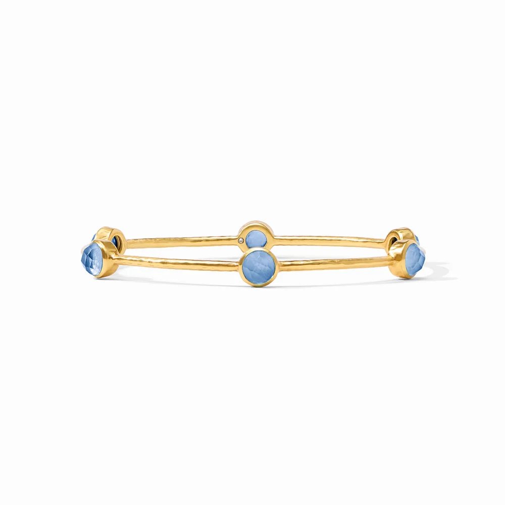 Gold bangle bracelet featuring four round blue gemstones against a white background.