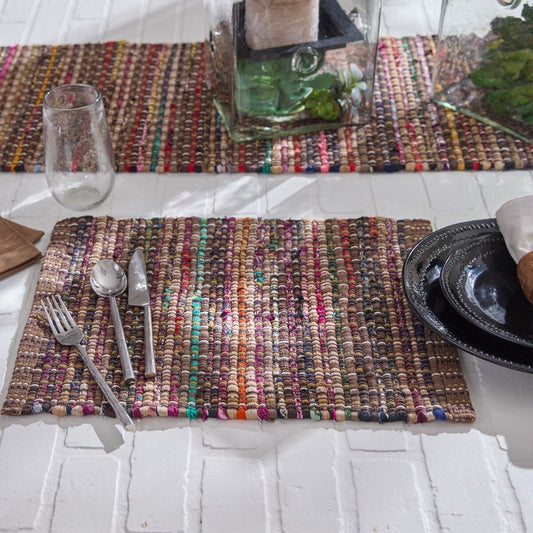 Colorful placemat with cutlery, glass, and dark plates on a white table.