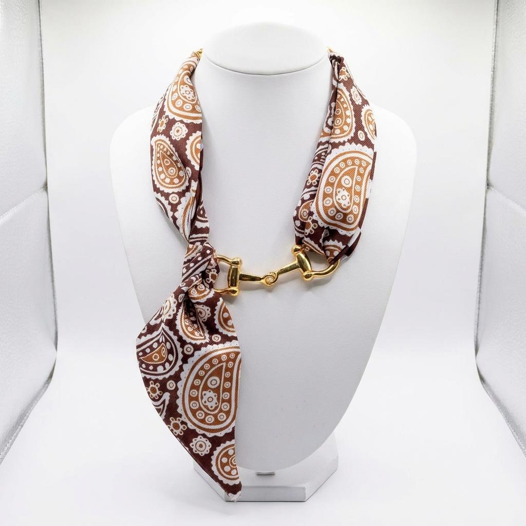 A brown paisley scarf is styled as a necklace with a gold-tone clasp on a white display bust.