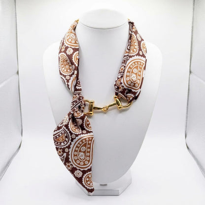 A brown paisley scarf is styled as a necklace with a gold-tone clasp on a white display bust.