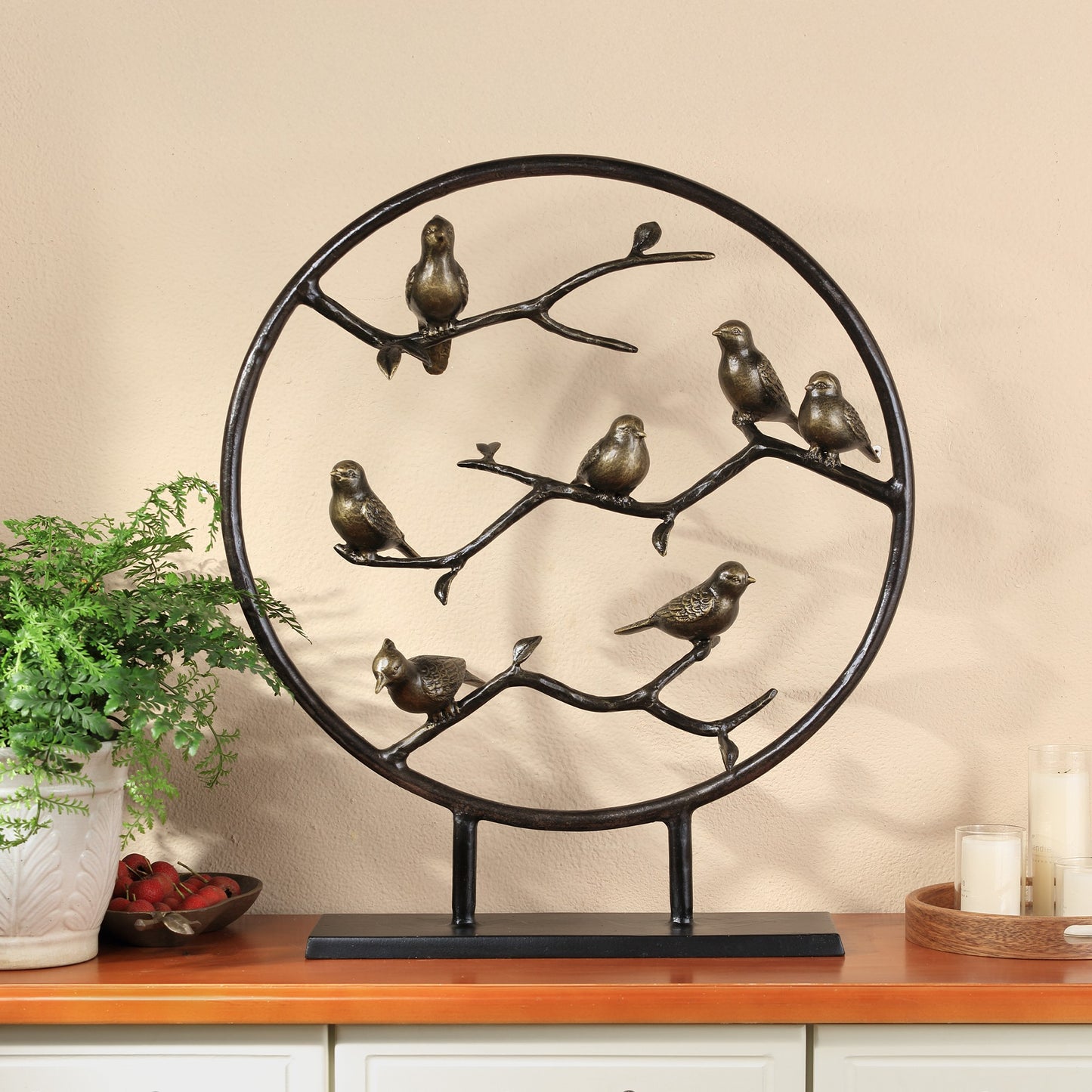 Metal bird sculpture on a branch inside a circular frame.