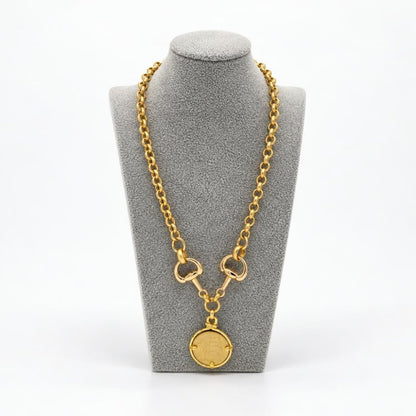 Gold chain necklace with a round pendant displayed on a gray jewelry bust.