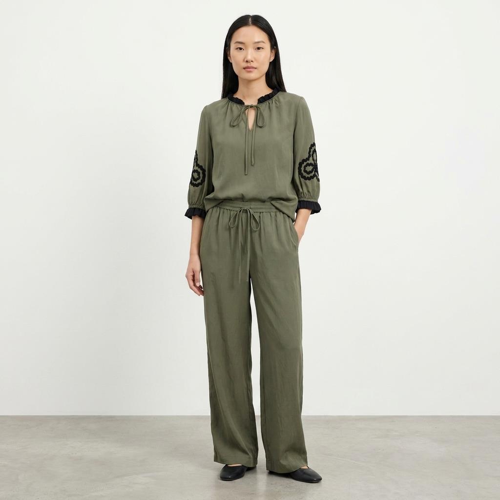 Person in olive outfit with black embroidery on the sleeves.