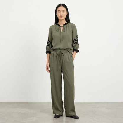 Person in olive outfit with black embroidery on the sleeves.