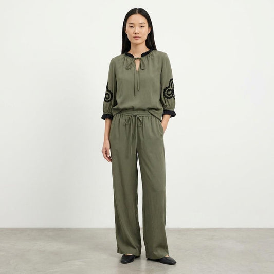 Person in olive outfit with black embroidery on the sleeves.