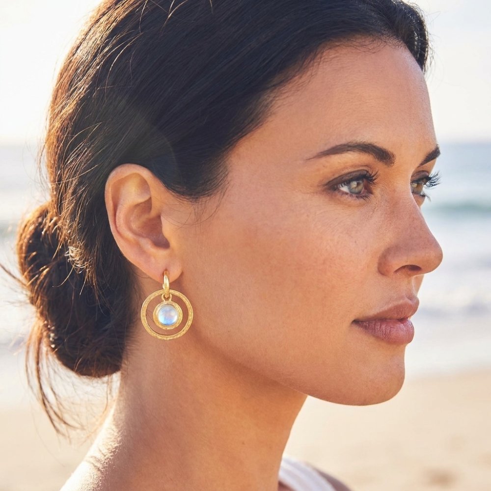 Close-up portrait of a woman wearing a gold hoop earring by the beach.