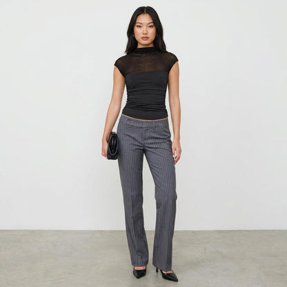 Woman in black top and pinstripe pants holds a clutch, standing confidently.