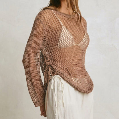 Woman in a brown mesh top and white pants against a light background.