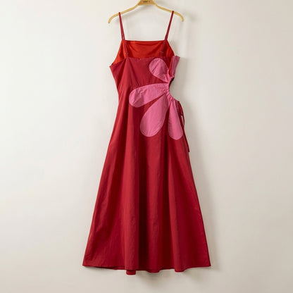 Red dress with pink flower design, hanging on a wooden hanger.