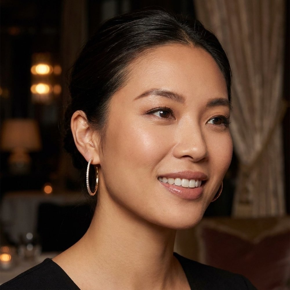 A smiling woman with dark hair and hoop earrings poses in a warmly lit room.