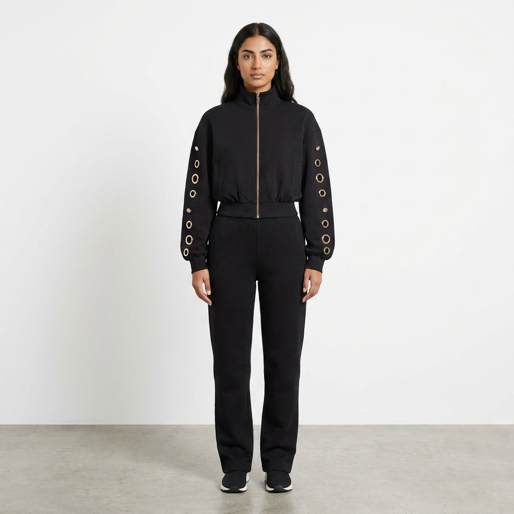 Woman in a black outfit with grommeted sleeves standing on a plain background.