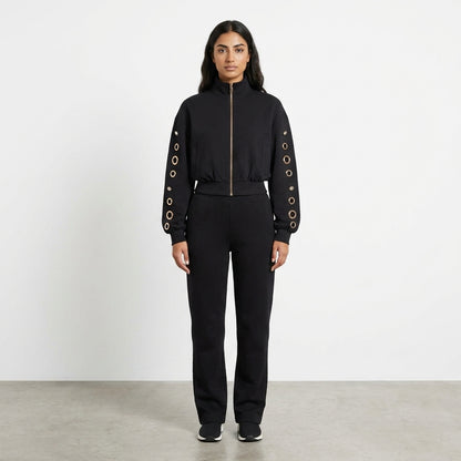 Woman in a black outfit with grommeted sleeves standing on a plain background.