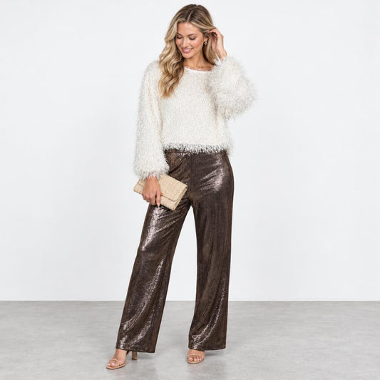 A woman models a fluffy white sweater with shiny brown wide-leg pants and a beige clutch.