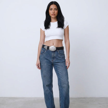 Woman in a white crop top and jeans with a large belt buckle.