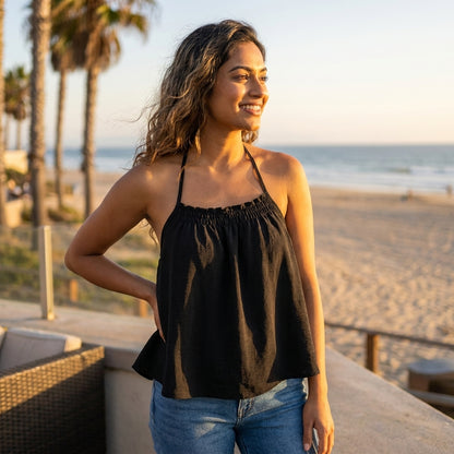 Smiling woman in black top enjoys a sunny beach view.