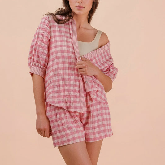 Person wearing a pink and white checkered pajama set against a beige background.