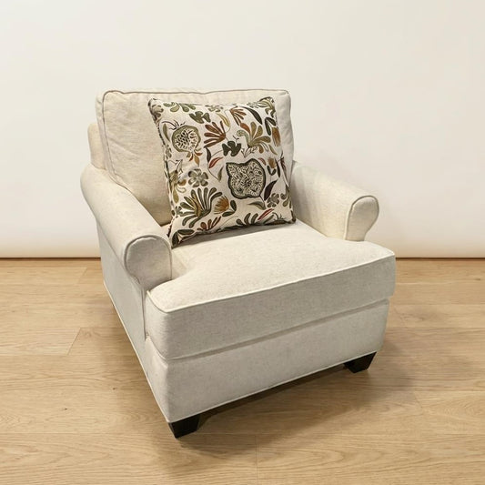 Cream armchair with floral cushion on wooden floor.