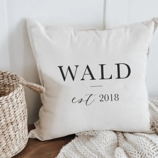 White pillow with "WALD est. 2018" text next to a woven basket.