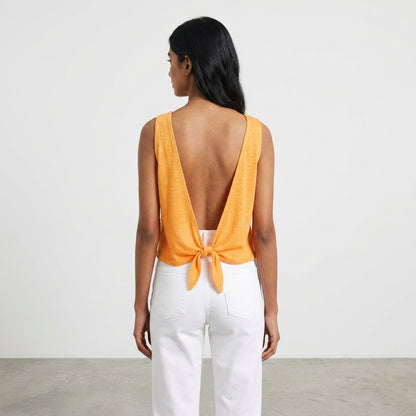 Woman in an orange top with open back and white pants.
