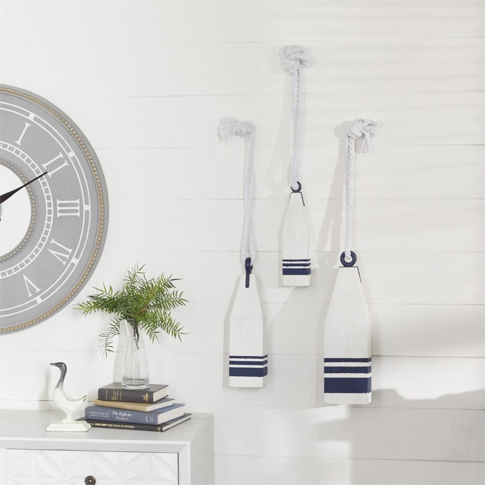 Wall decor with nautical paddles, clock, books, and plant.