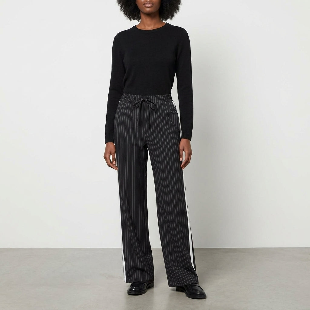 Person in black sweater and striped pants standing against a plain background.