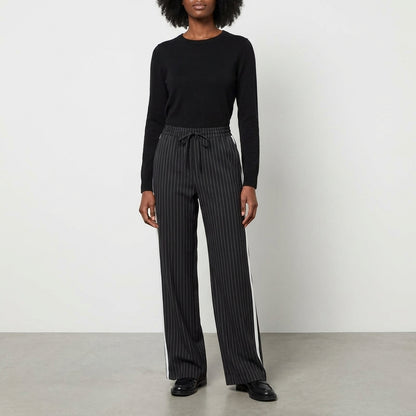 Person in black sweater and striped pants standing against a plain background.