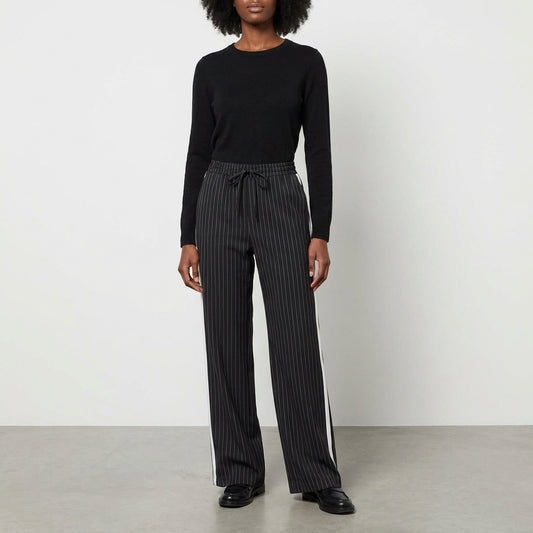 Person in black sweater and striped pants standing against a plain background.