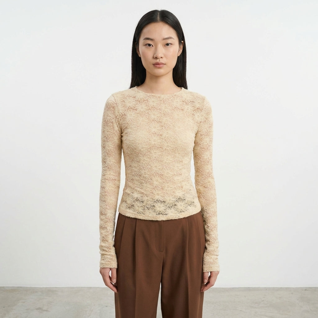 Person in beige lace top and brown pants against a white background.