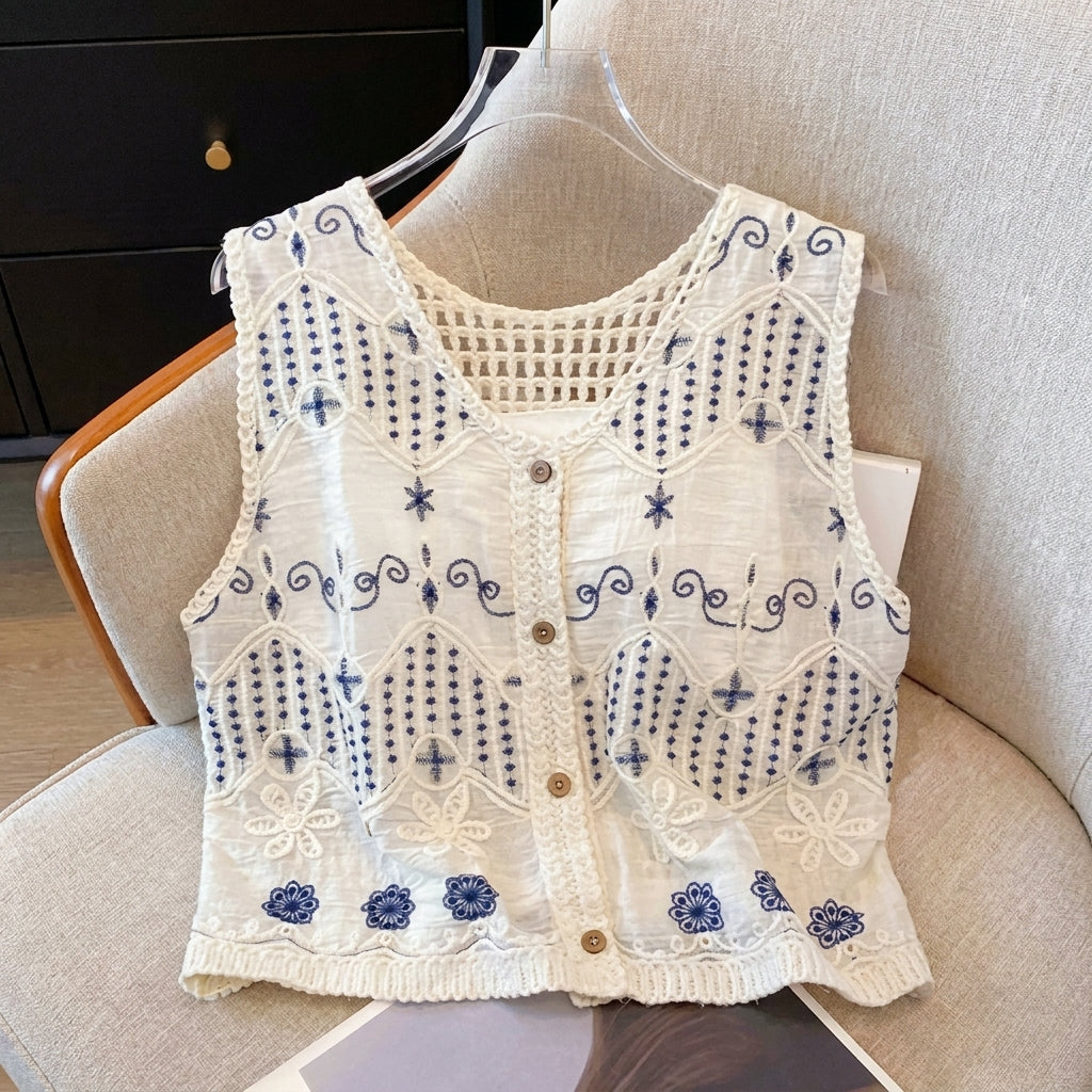 White embroidered vest with blue floral patterns displayed on a beige chair.