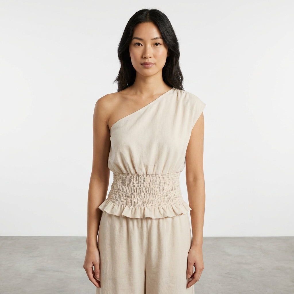 Person in a beige one-shoulder outfit, standing against a plain background.