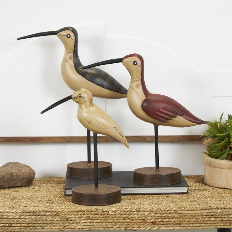 Three wooden bird sculptures on stands in a room.