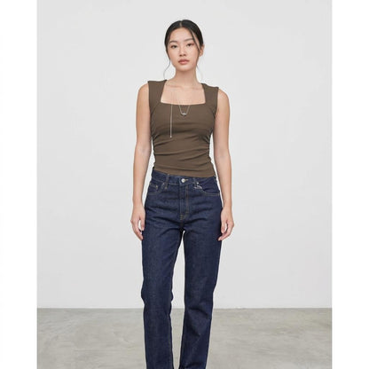 Woman in a brown sleeveless top and jeans against a plain backdrop.
