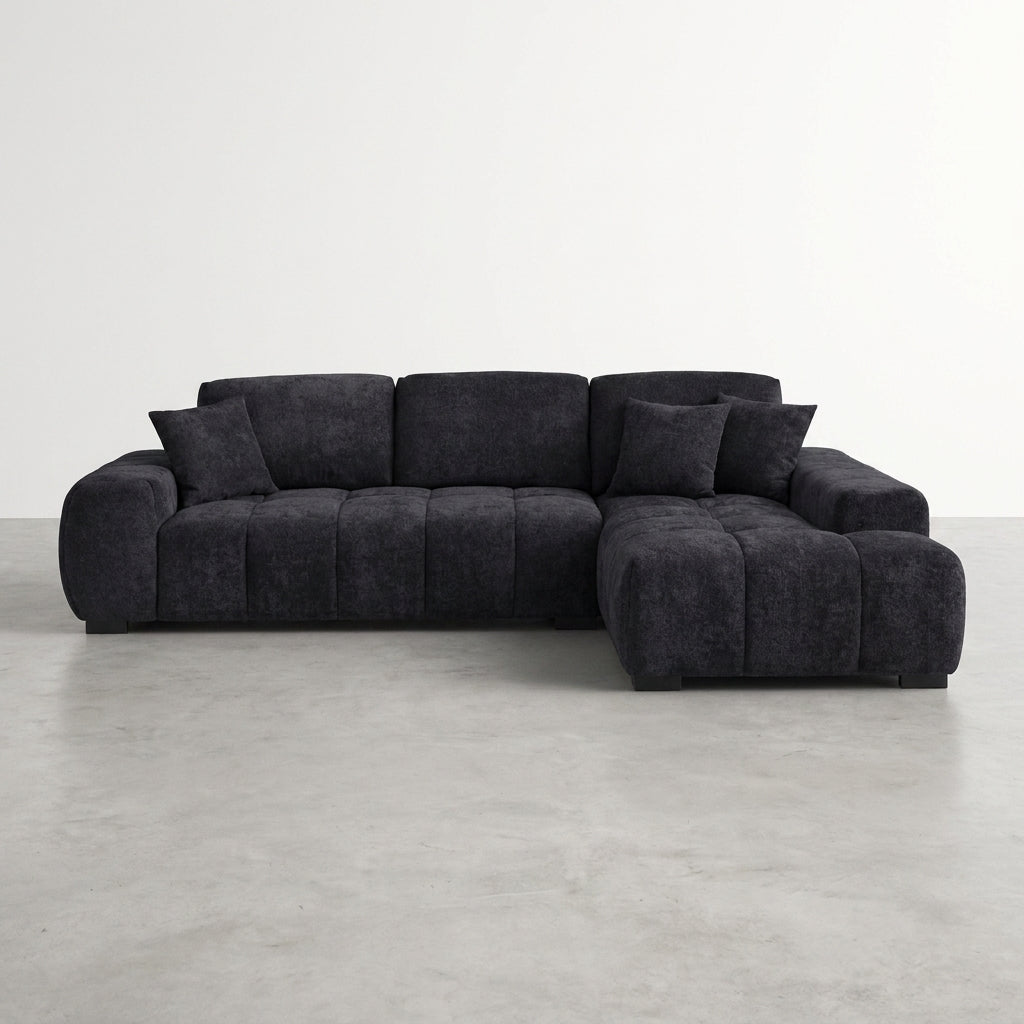 Dark gray sectional sofa with plush pillows on a concrete floor.