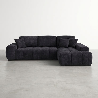 Dark gray sectional sofa with plush pillows on a concrete floor.