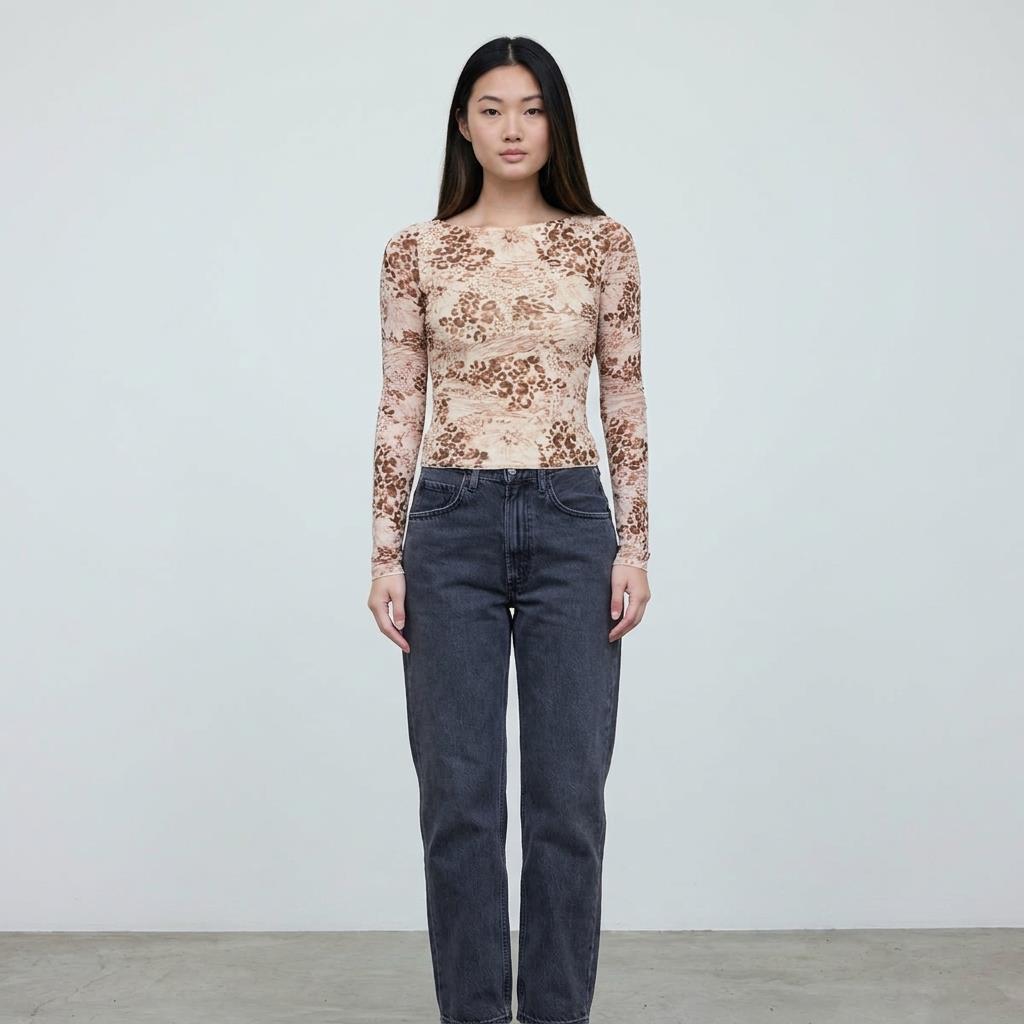 Person in printed top and jeans standing against a plain background.