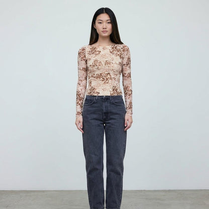 Person in printed top and jeans standing against a plain background.