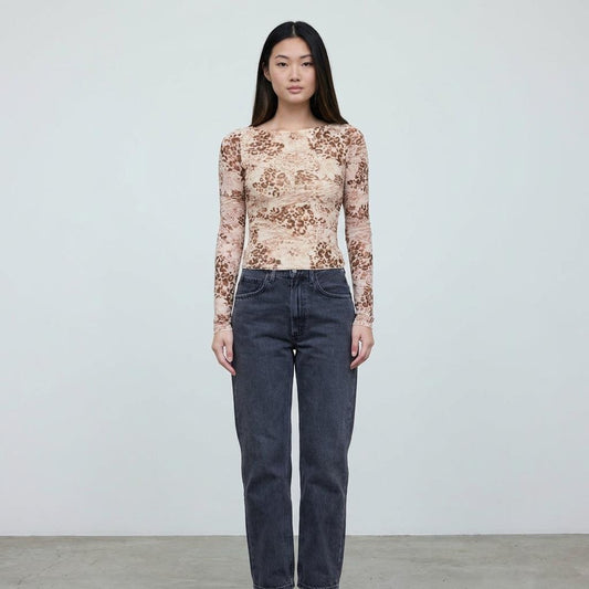 Person in printed top and jeans standing against a plain background.